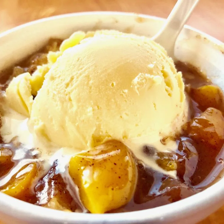 Peach cobbler under a scoop of vanilla ice cream