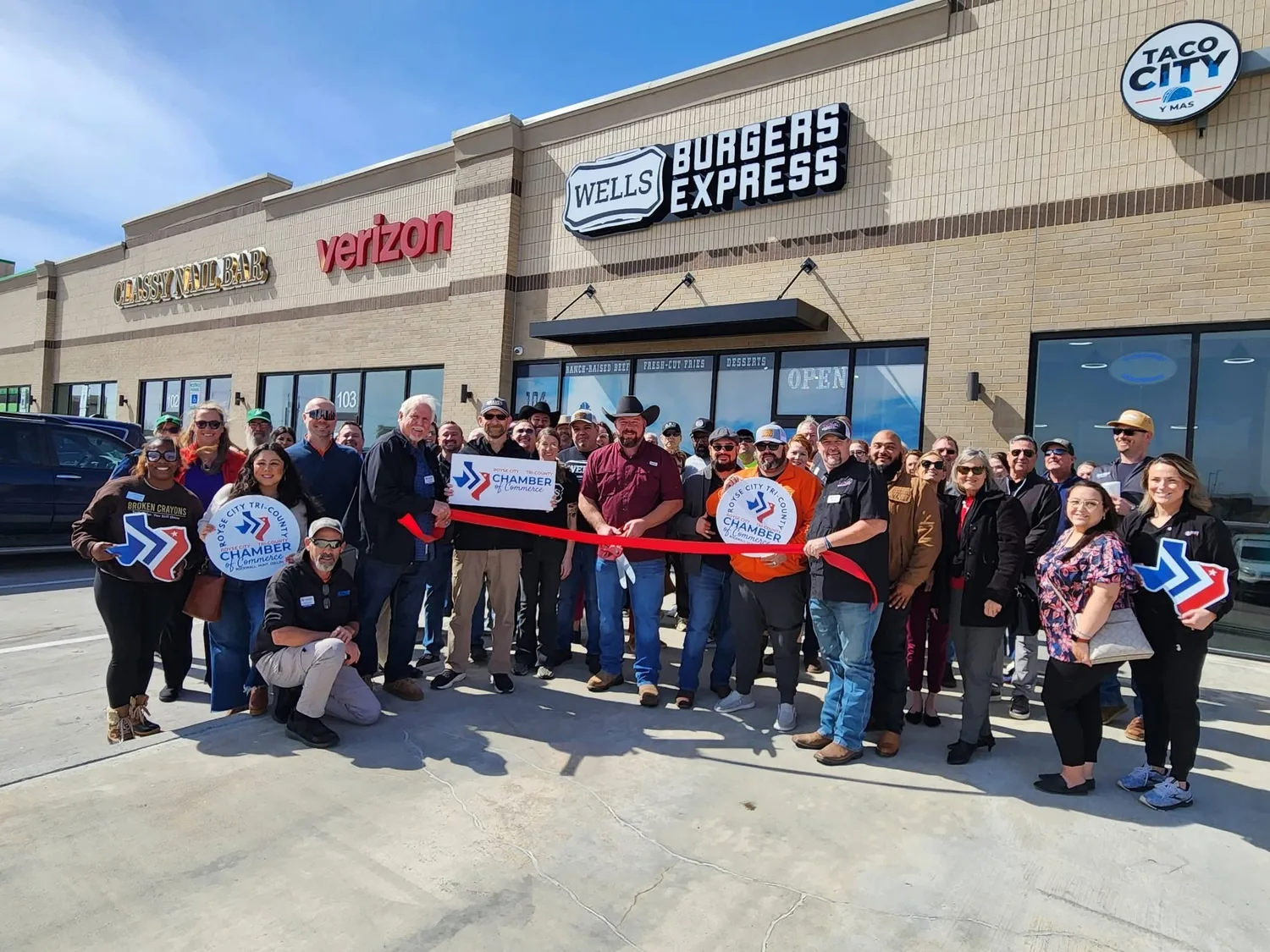 Ribbon cutting under the Wells Burgers Express sign with the Royse City chamber