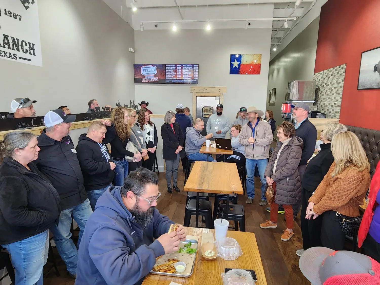 Opening day inside Wells Burgers Express, a room full of guests under the menu boards